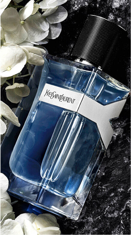 YSL Y Eau de Toilette bottle, with elegant white flowers and a dark,  luxurious textured background.
