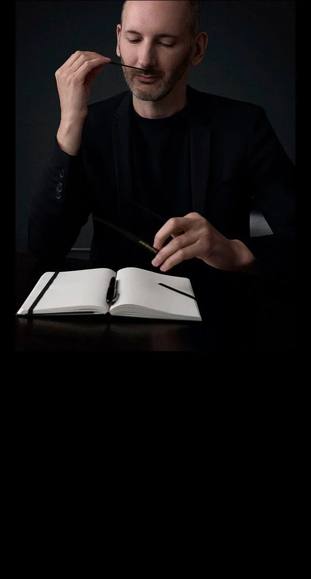 Quentin Bisch, perfumer, intently smelling a scent strip, with a notebook on a table.