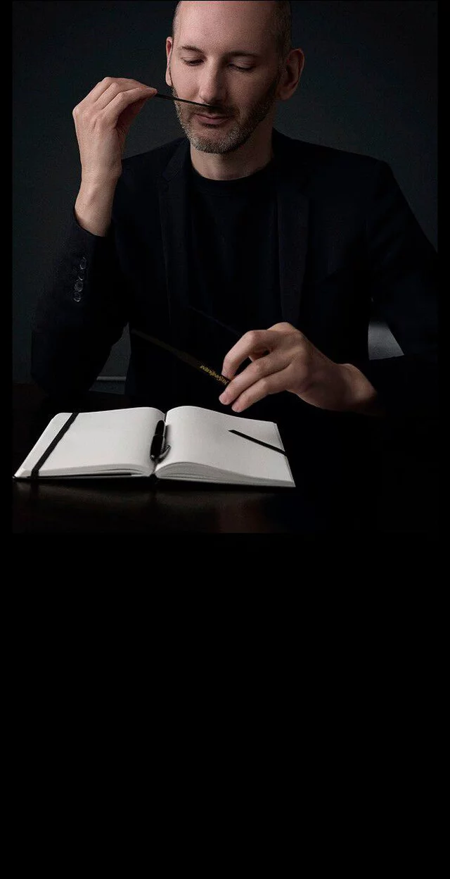 Quentin Bisch, perfumer, intently smelling a scent strip, with a notebook on a table.