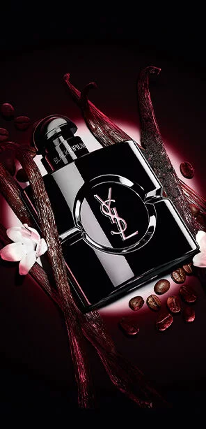 Black Opium Le Parfum bottle in glossy black, surrounded by dark vanilla pods and white jasmine.