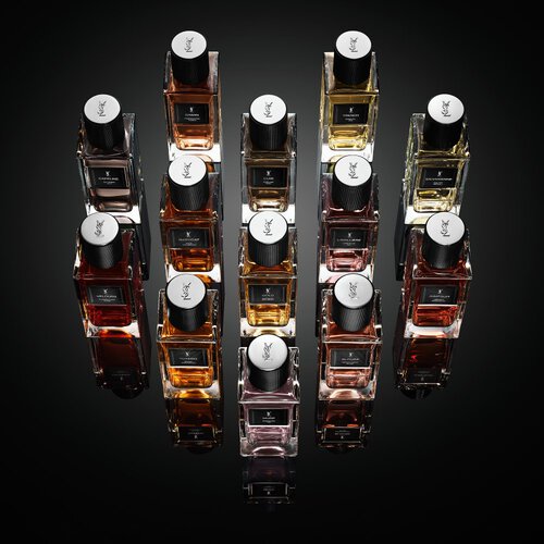 Full collection of YSL Le Vestiaire des Parfums fragrances in clear bottles with black caps, showcasing diverse liquid hues, on a reflective black surface.