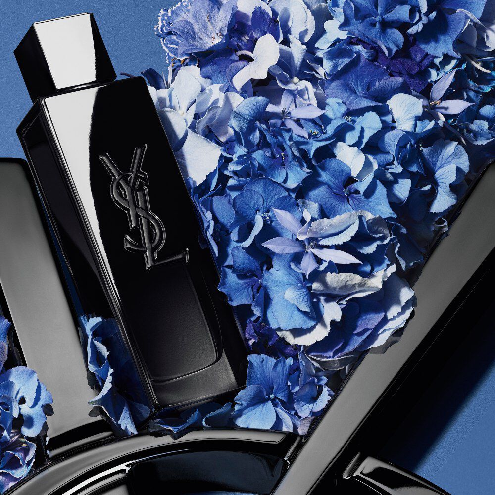 YSL MYSLF Eau de Parfum bottle on a glossy black YSL logo, with vibrant blue hydrangeas, against a deep blue background.