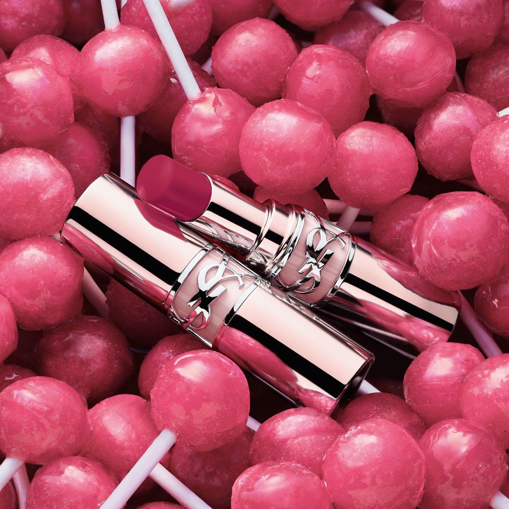 YSL LOVESHINE CANDY GLOW lip balm shade 11B Berry Lolly packshot placed among pink candy lollipops.