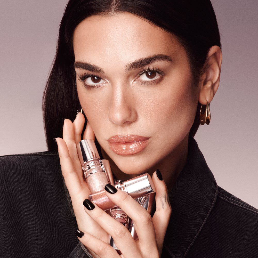 Dua Lipa holding multiple YSL Loveshine lipstick tubes near her face, showcasing luminous glossy lips.