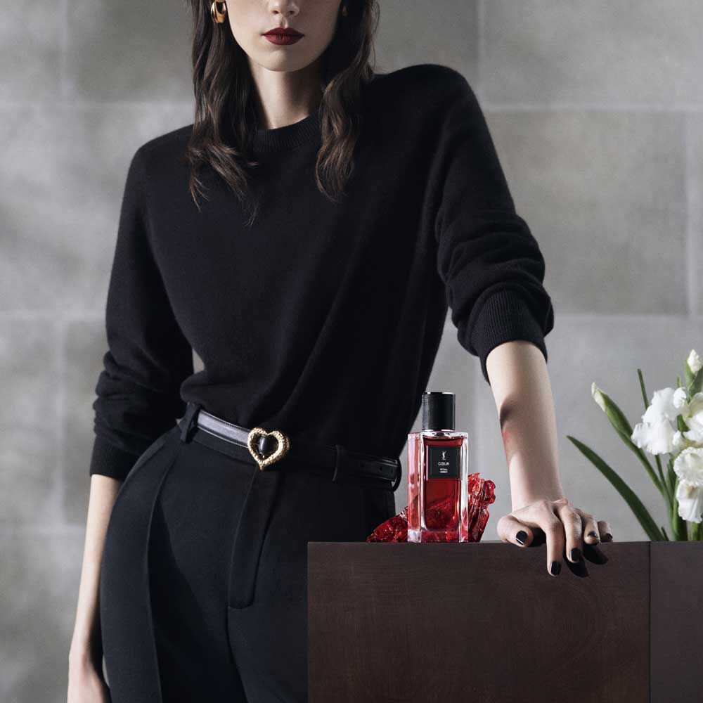 A model's dressed in black, posing next to the COEUR fragrance bottle for YSL Beauty.