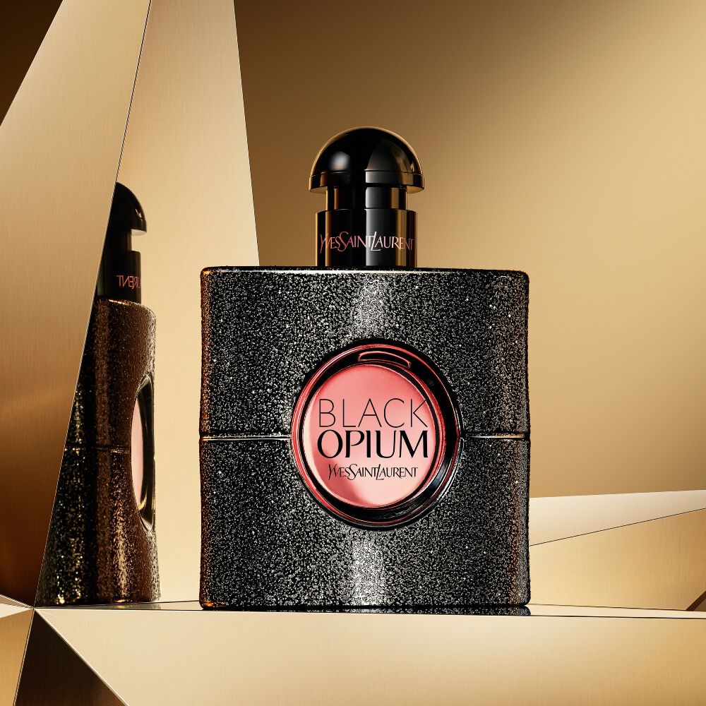 Black Opium eau de parfum bottle displayed on a reflective golden background.