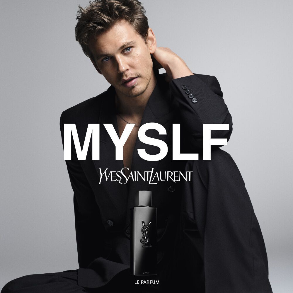 Austin Butler posing in a black suit for the MYSLF campaign with the MYSLF Le Parfum bottle in the foreground.