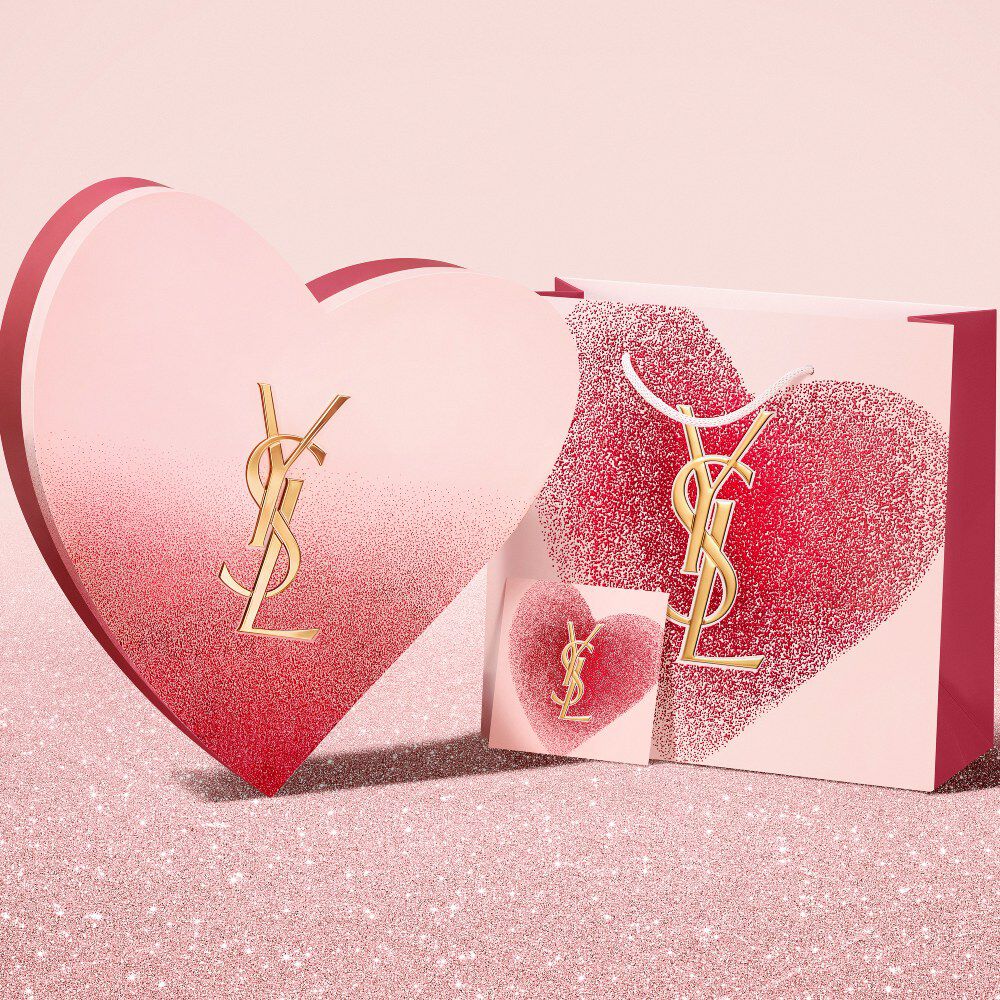 YSL Beauty Valentine's Day heart-shaped gift box,  gift card, and shopping bag on a red glitter background.