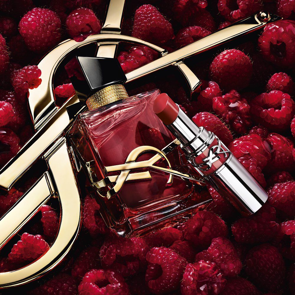 Libre Eau de parfum Berry Crush and Loveshine lipstick in Berry Crush, with the Cassandre logo, on a bed of raspberries.