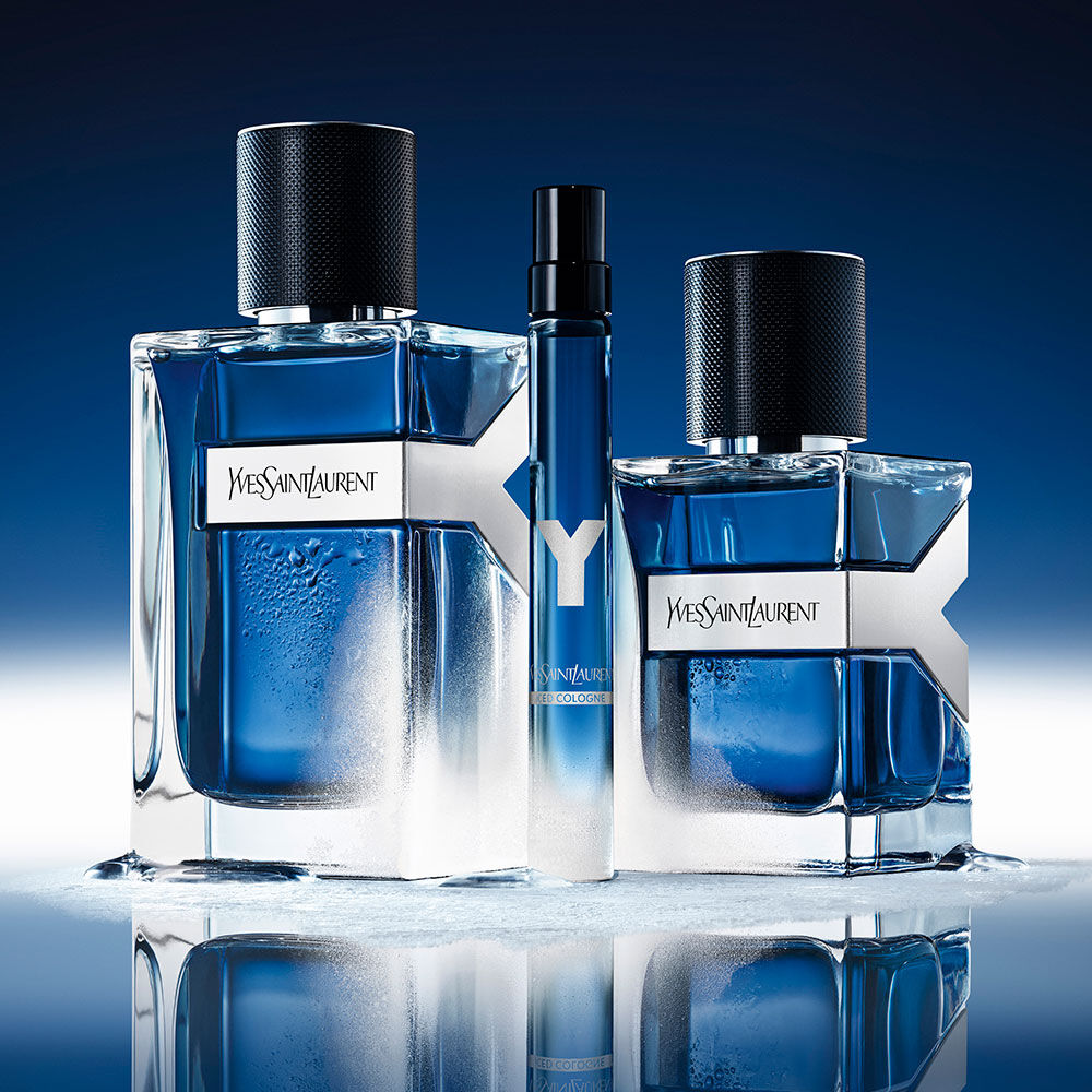 YSL Y Eau de Toilette Intense Iced Cologne trio: 100ml, 60ml, and 10ml bottles, frosted with water droplets, on a reflective blue surface.