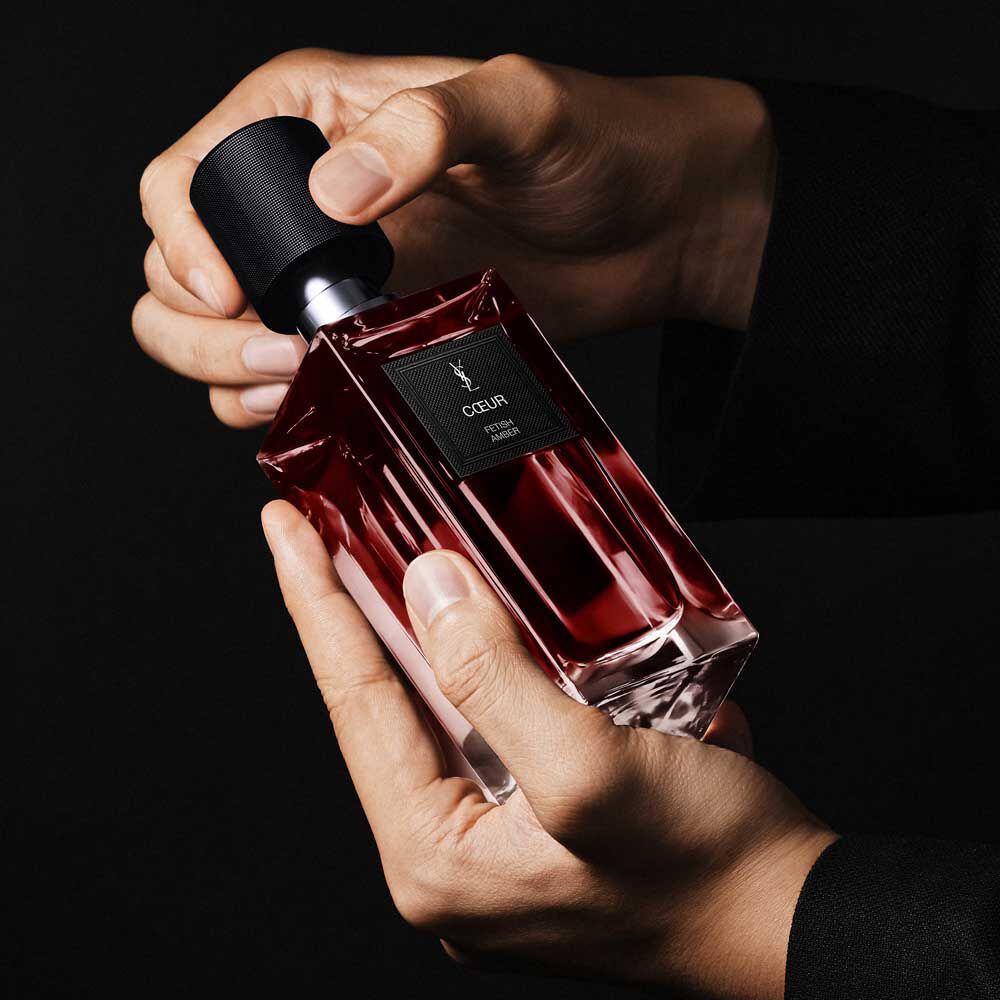 Hands holding the COEUR Eau de Parfum ruby-red bottle to demonstrate the YSL Art of Application and couture design.