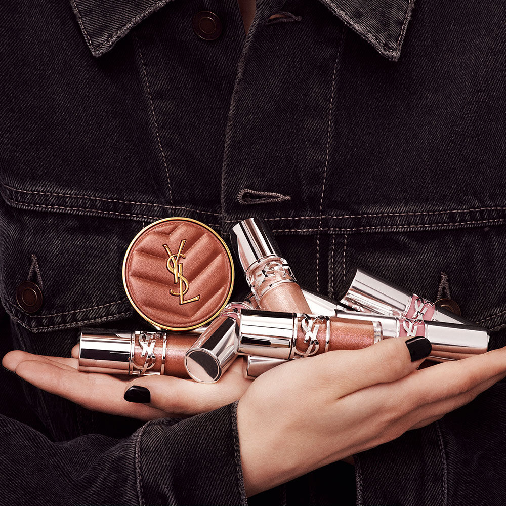 Hands holding YSL LOVESHINE Plumping Lip Oil Gloss and Make Me Blush, showcasing luxury beauty products.