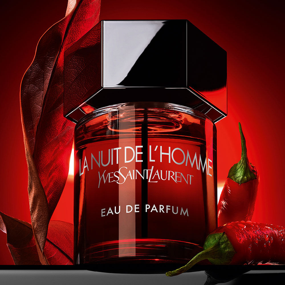 The La Nuit de l’Homme Eau de Parfum bottle paired with a red chili pepper and a dry leaf, representing its spicy and incandescent scent.