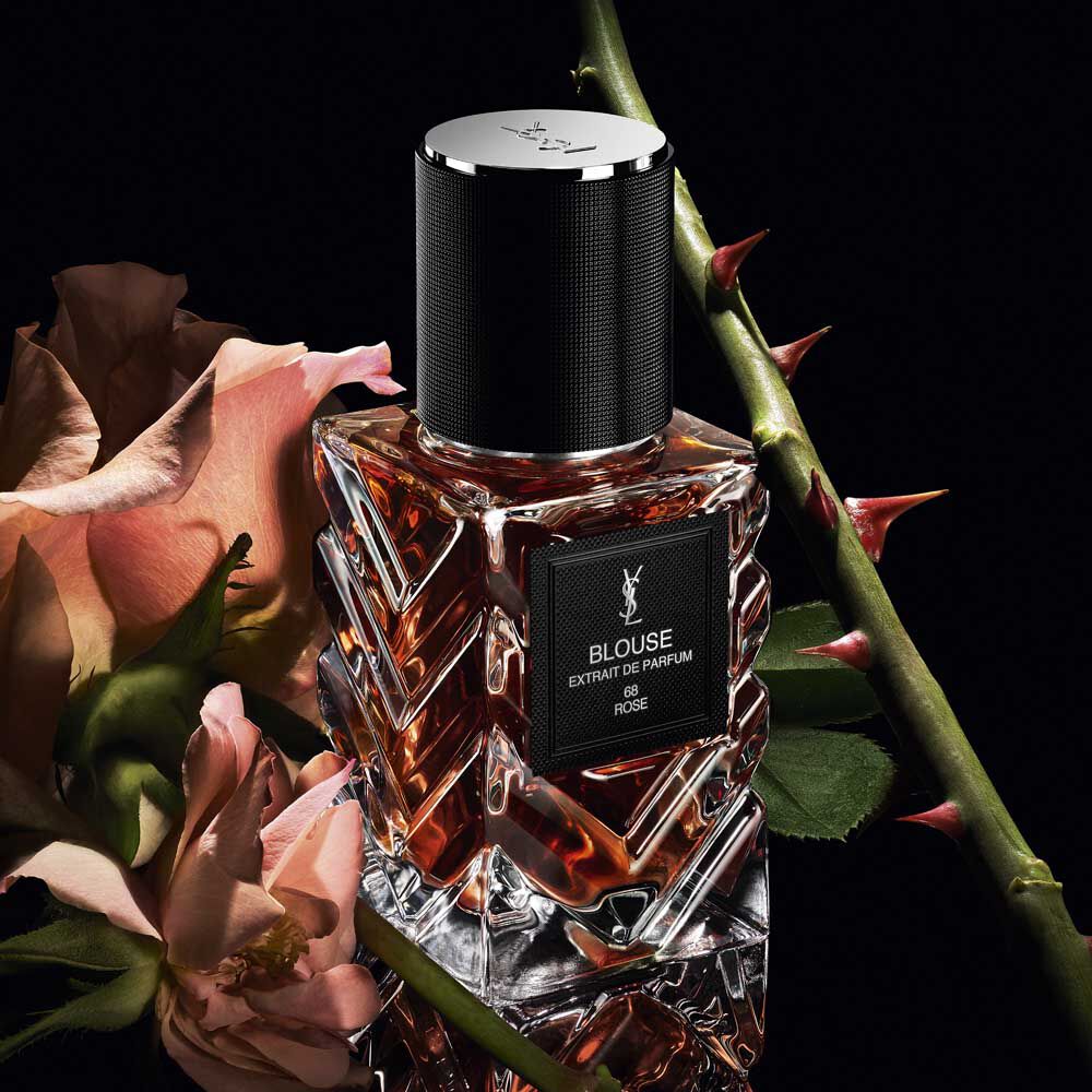 Three-quarter view of YSL LVDP Blouse Extrait de Parfum bottle, with pink roses and thorny stems on a dark background.