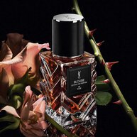 Three-quarter view of YSL LVDP Blouse Extrait de Parfum bottle, with pink roses and thorny stems on a dark background.