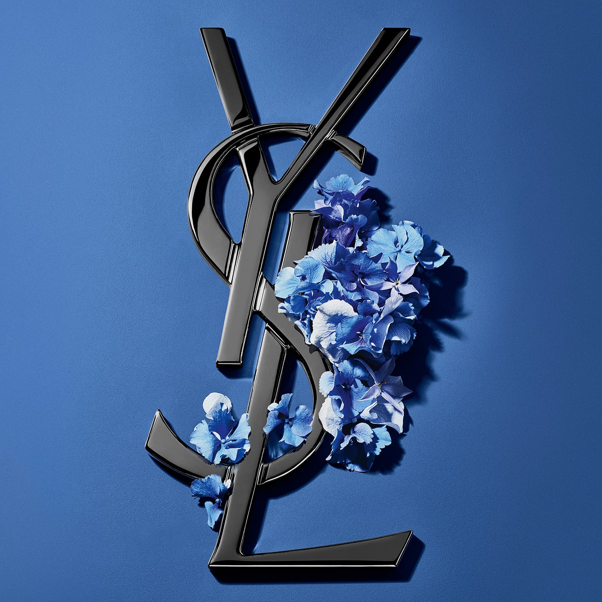 Black YSL Cassandre logo adorned with vibrant blue
spring flowers, set against a serene blue
background.