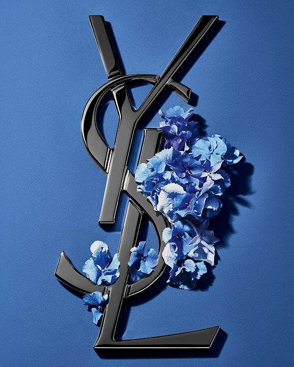 Black YSL Cassandre logo adorned with vibrant blue
spring flowers, set against a serene blue
background.