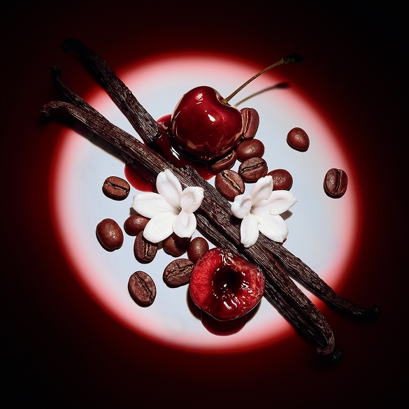 Close-up of juicy red cherries, jasmine flowers, vanilla pods, and coffee beans highlighted by a dramatic spotlight for Black Opium Eau de Parfum Over Red.