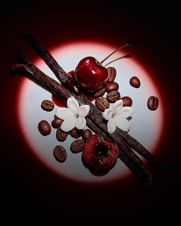 Close-up of juicy red cherries, jasmine flowers, vanilla pods, and coffee beans highlighted by a dramatic spotlight for Black Opium Eau de Parfum Over Red.