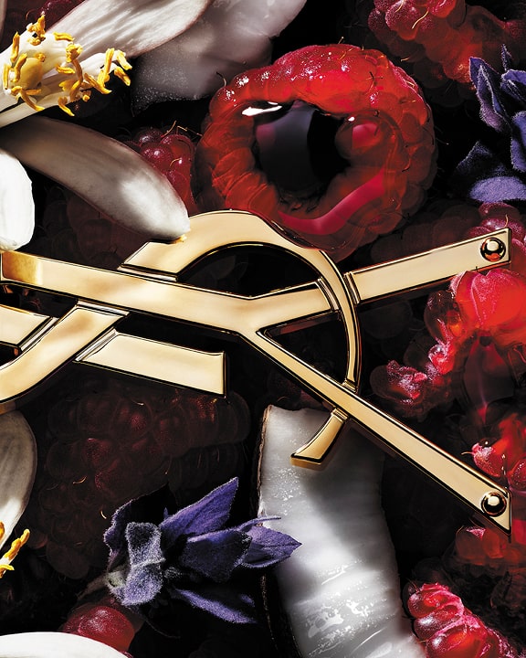 Close-up of raspberries and white flowers with a gold YSL Cassandre detail, evoking the fruity floral notes of LIBRE Berry Crush.