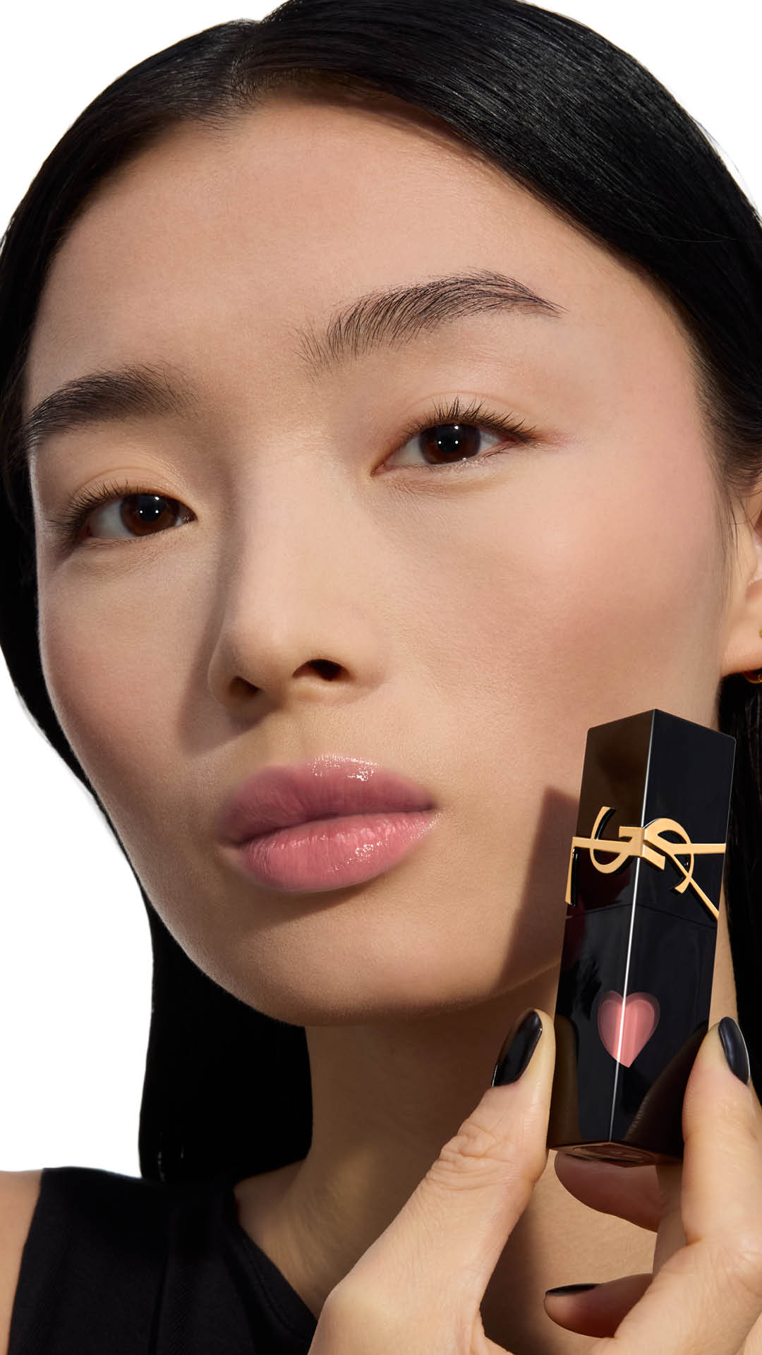 Light skin tone model showcasing a soft, glossy pale pink lip shade while holding a YSL THE INKS VINYL CREAM lip stain bottle next to her cheek.