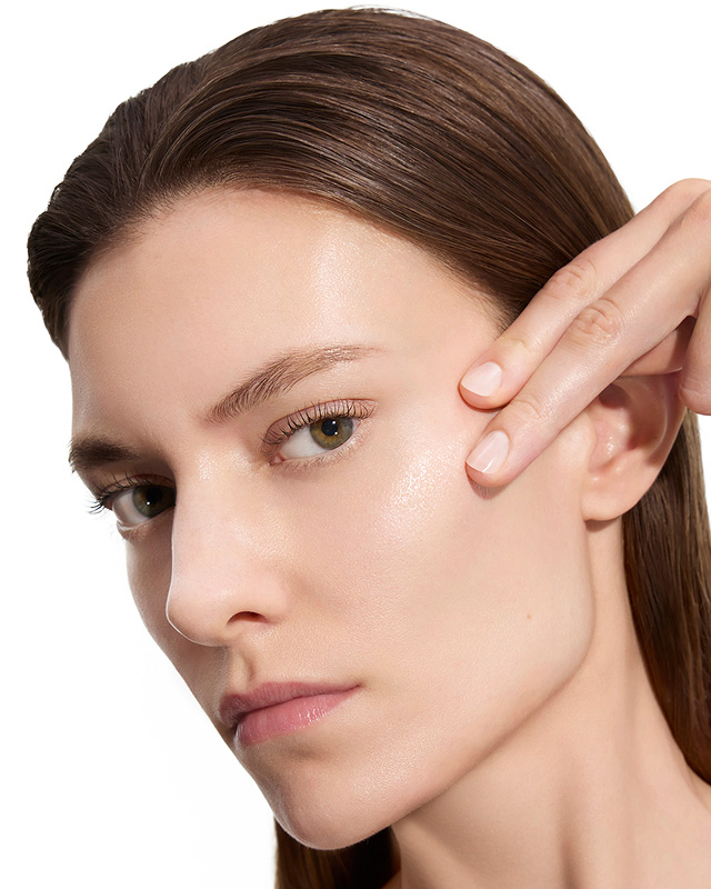 Marije, YSL Beauty model, with fair skin, gently touching her cheek, showcasing smooth skin after lotion application.