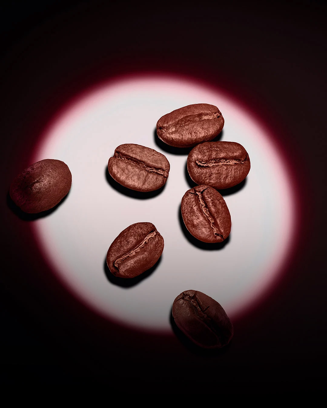 A group of roasted coffee beans highlighted by a pink circular spotlight on a dark background. 