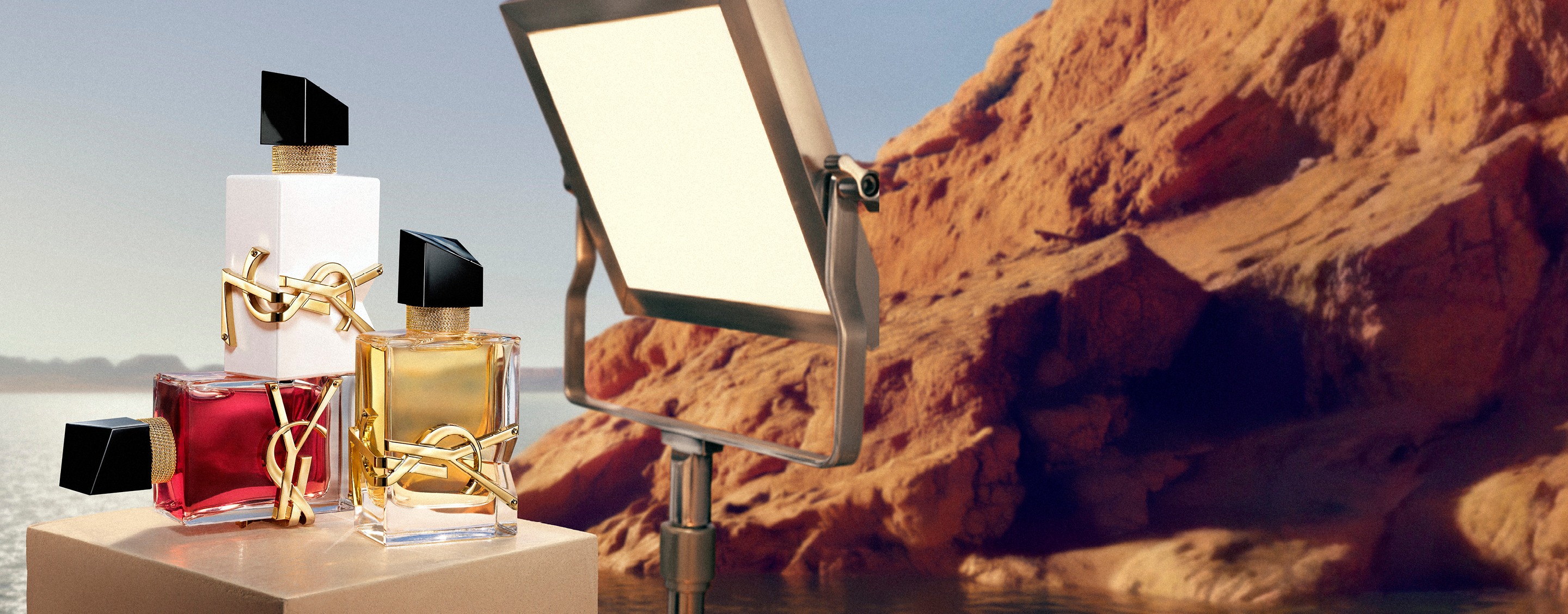 YSL LIBRE EDP, LIBRE EAU NUE, and LIBRE BERRY CRUSH perfumes on a pedestal with studio light in a desert landscape.