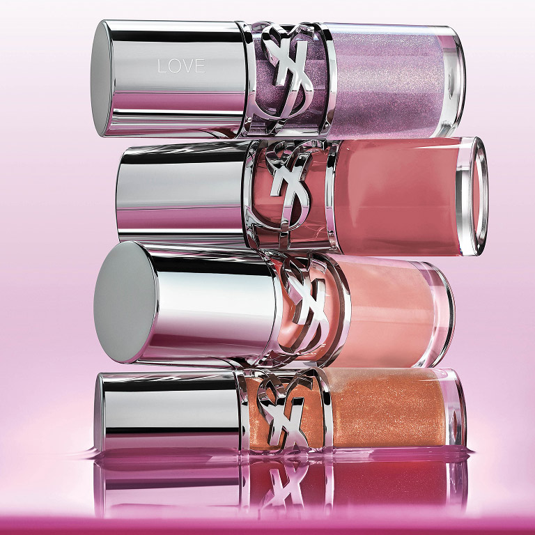 Four YSL LOVESHINE Plumping Glosses in diverse shades stacked, reflecting on a pink surface.
