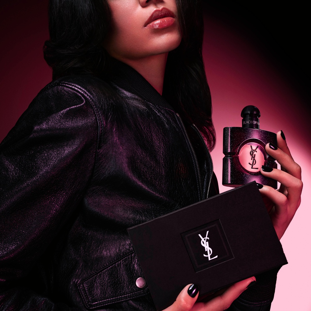A women model in a leather jacket holding a Black Opium Eau de Parfum bottle and a black YSL gift box.