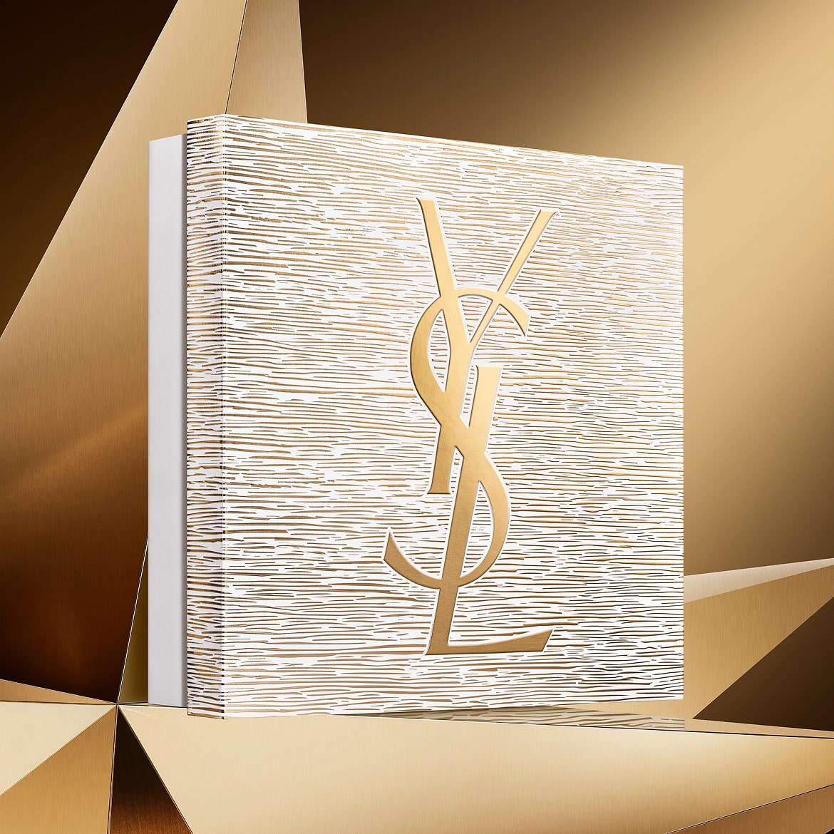 Holiday gift set in gold tones, featuring the YSL Beauty logo, on a golden geometric background.