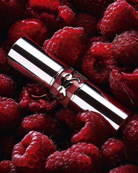 YSL LOVESHINE Berry Crush lipstick, silver tube with berry YSL logo, nestled among fresh raspberries.