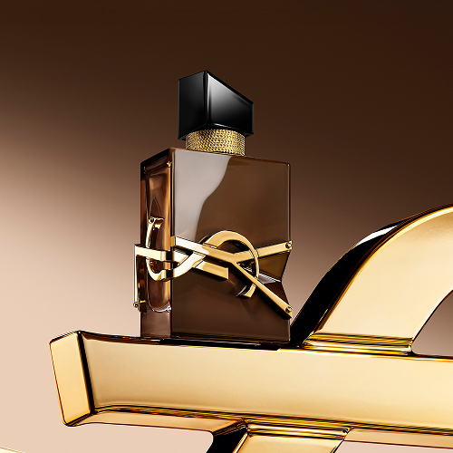 Glazed brown Libre Santal Couture bottle reflecting light, placed on a large golden YSL Cassandre.