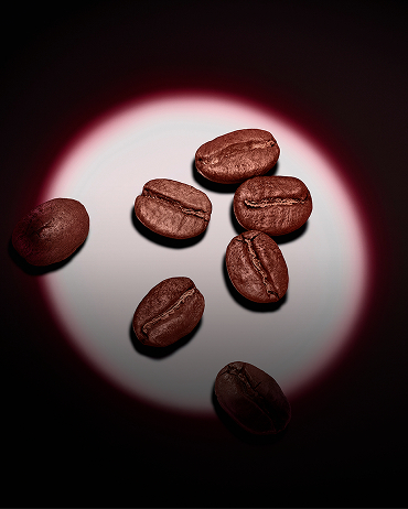 A group of roasted coffee beans highlighted by a pink circular spotlight on a dark background.