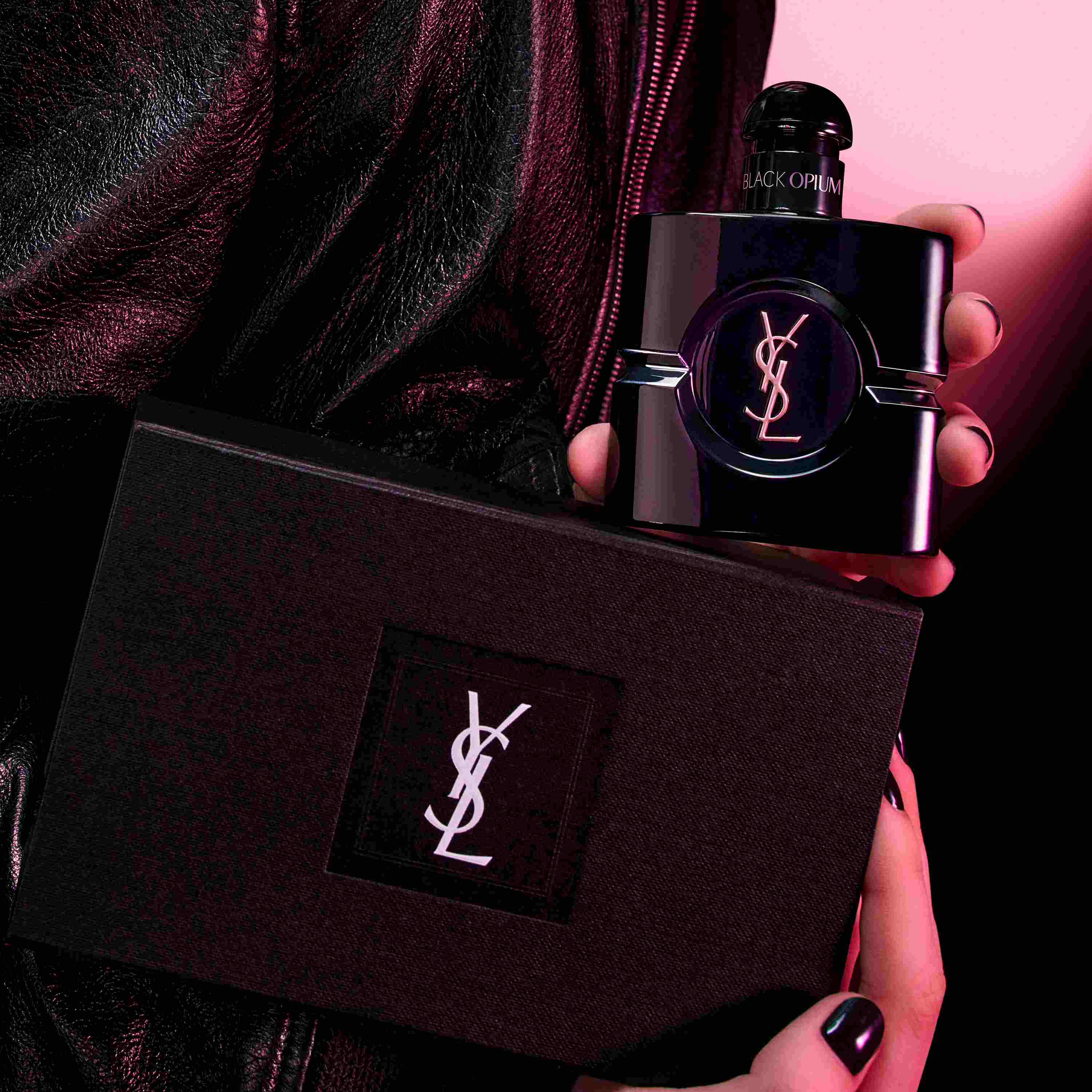 Close-up of a model in a black leather jacket holding the glossy Black Opium Le Parfum bottle and an exclusive YSL gift box.