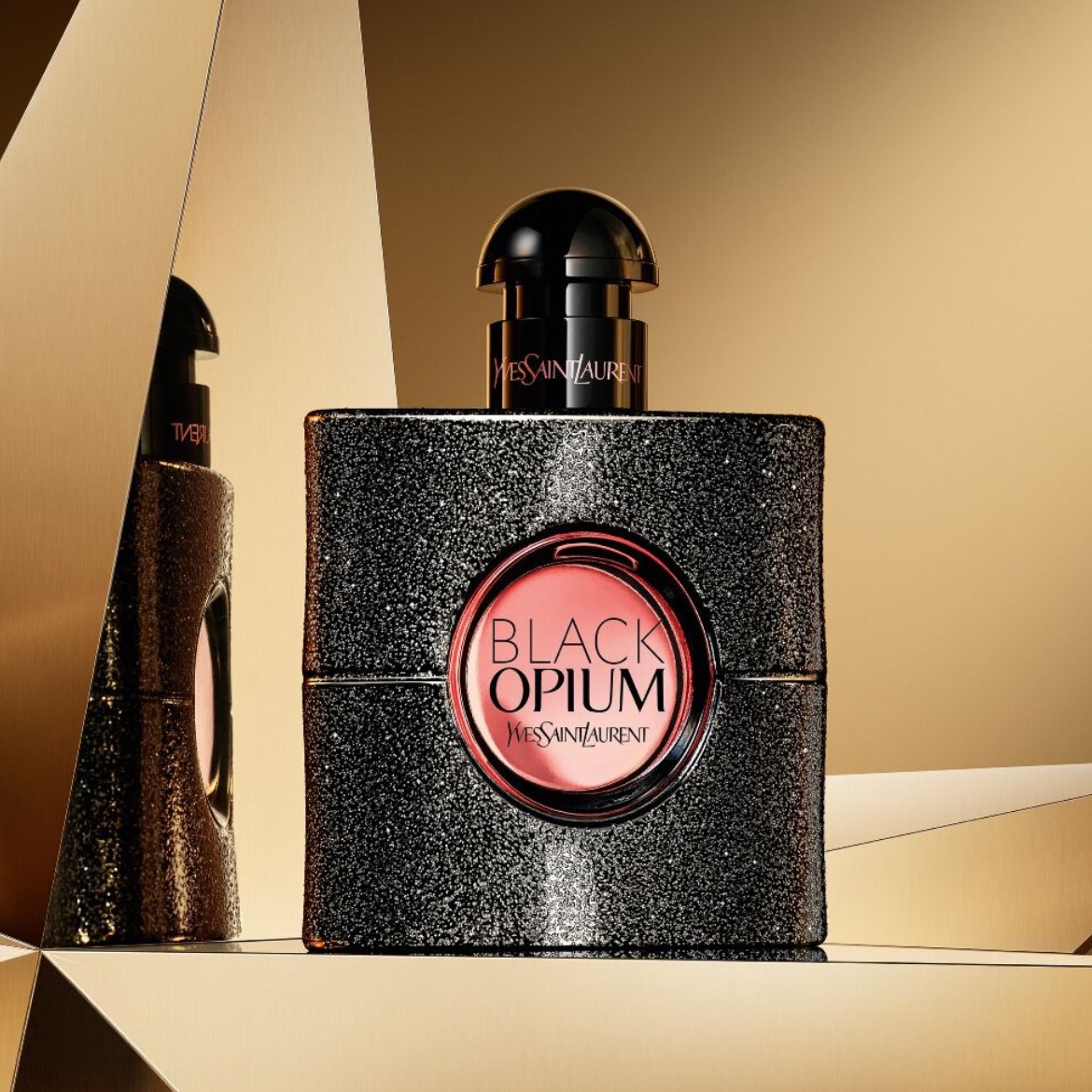 Black Opium eau de parfum bottle displayed on a reflective golden background.