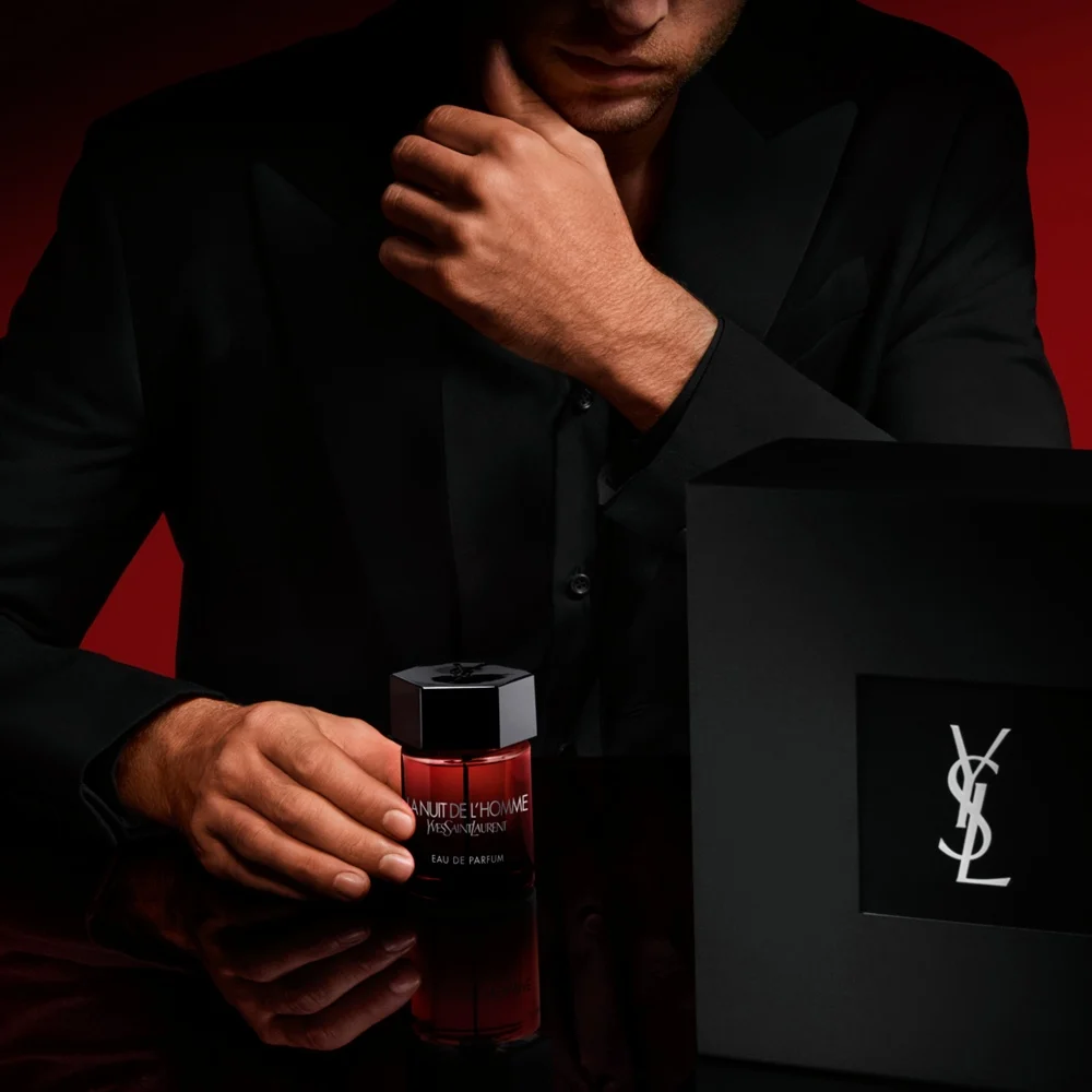 Hands holding a YSL Loveshine in shade 44, with "HOLIDAY" engraved on the cap, against a golden background.