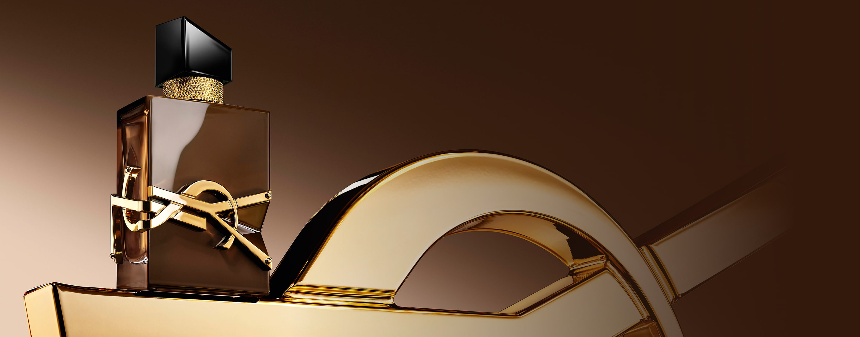 Glazed brown Libre Santal Couture bottle reflecting light, placed on a large golden YSL Cassandre.