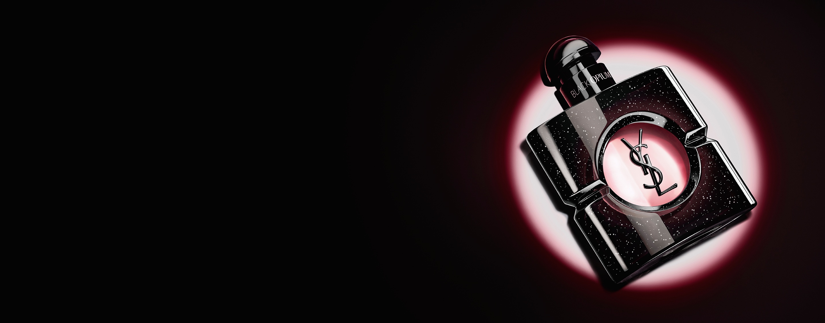 Black Opium Eau de parfum bottle lying on its side on a dark surface with a pink light halo.