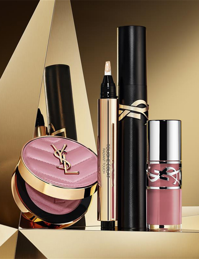 Make Me Blush powder in shade 44, Stylo Touch Eclat, Lash Clash mascara, and YSL Loveshine Plumping Lip Oil Gloss shade 12, on a golden geometric background.