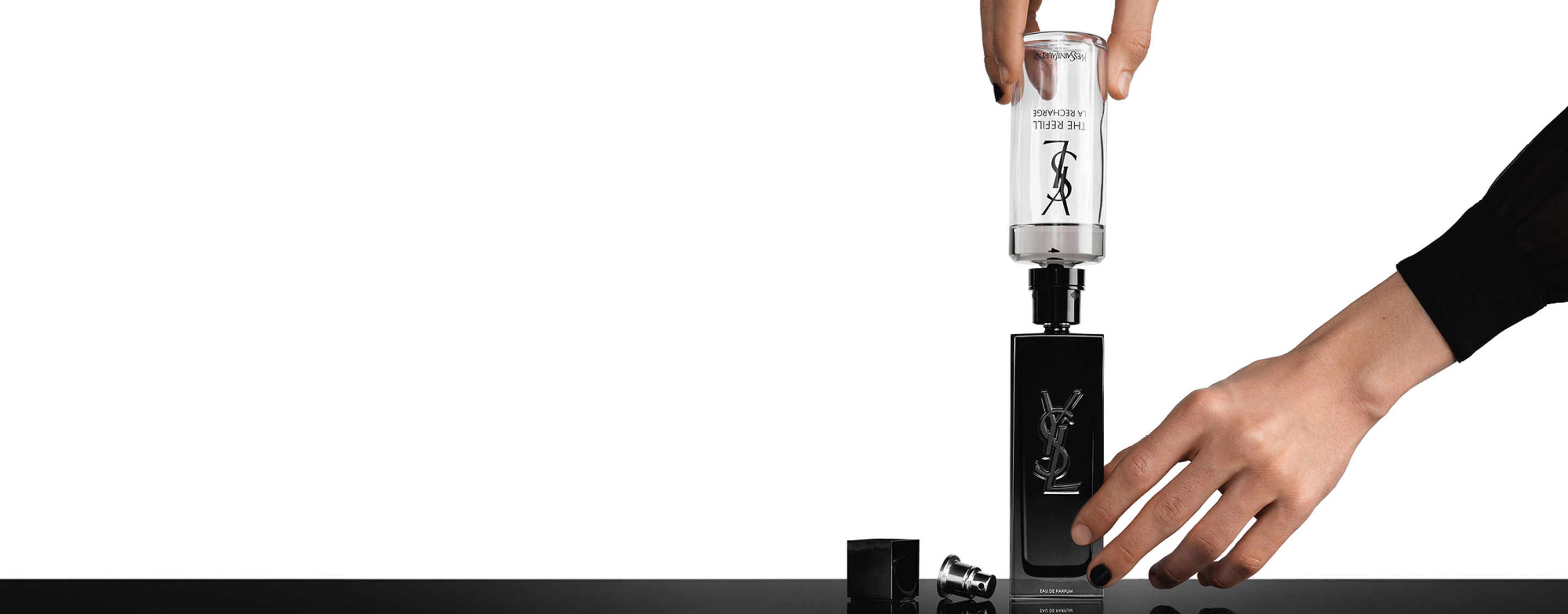 A large, transparent glass refill bottle is shown pouring fragrance into a standard matte black MYSLF bottle.