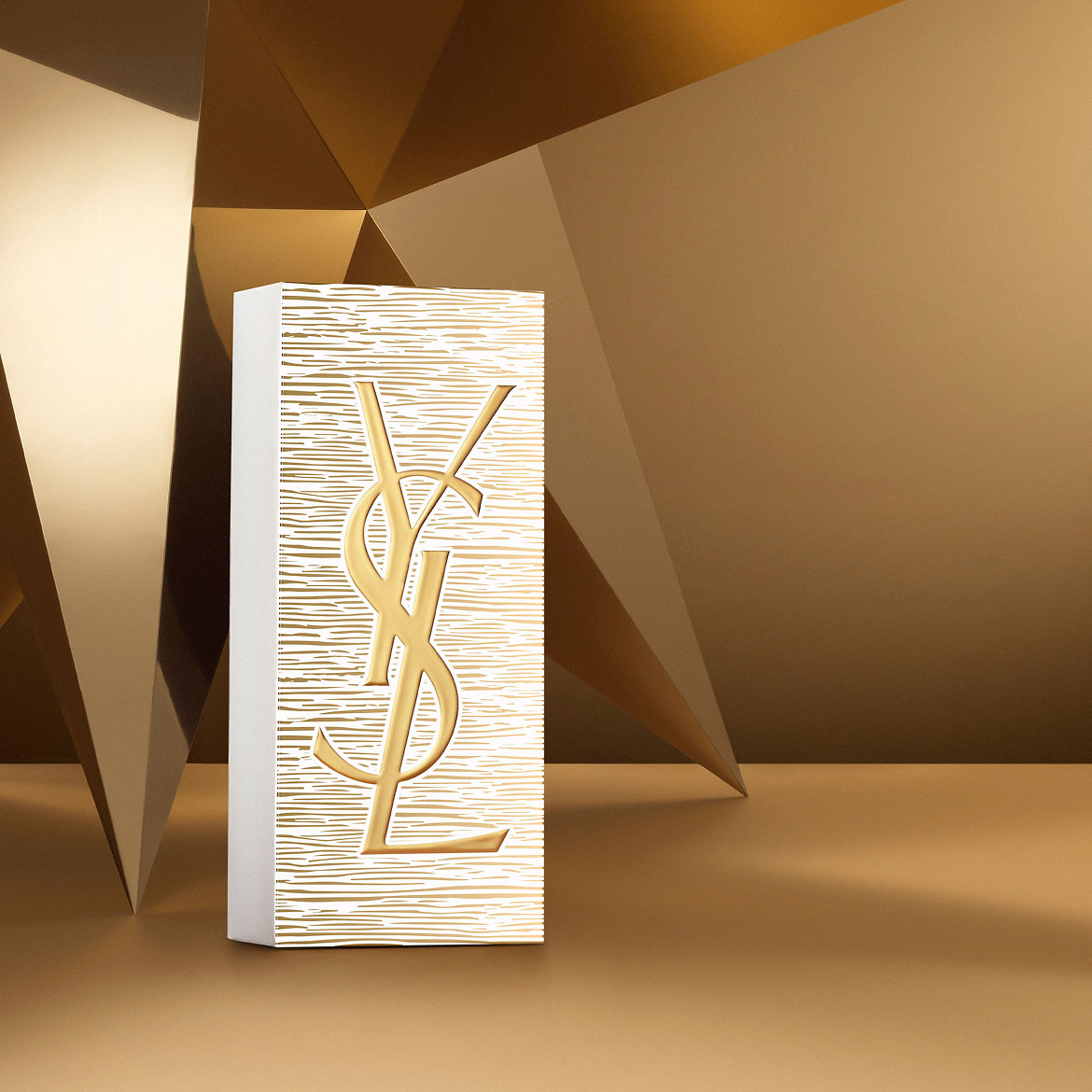 YSL Beauty Holiday gift set box in gold and white, featuring the YSL Beauty logo, on a golden geometric background.