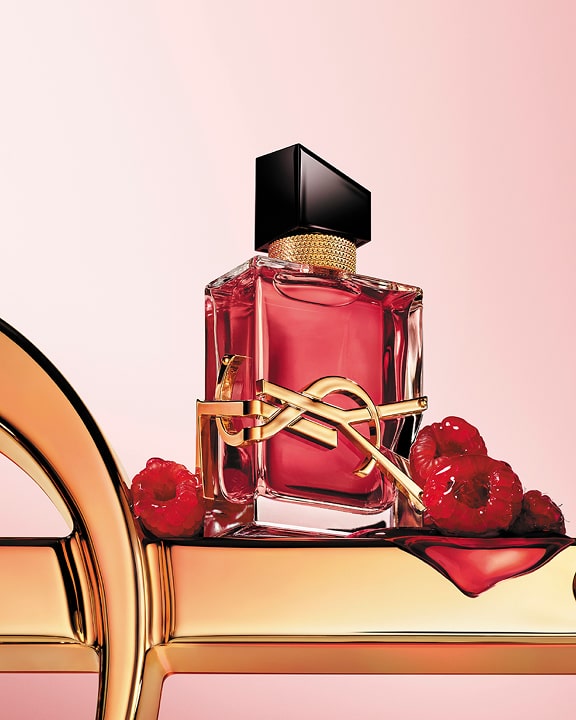 LIBRE Berry Crush berry-red perfume bottle with gold YSL Cassandre logo, styled with raspberries on a soft pink background.