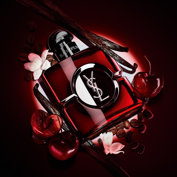 Black Opium Over Red bottle in deep red lacquer surrounded by fresh red cherries and roasted coffee beans.