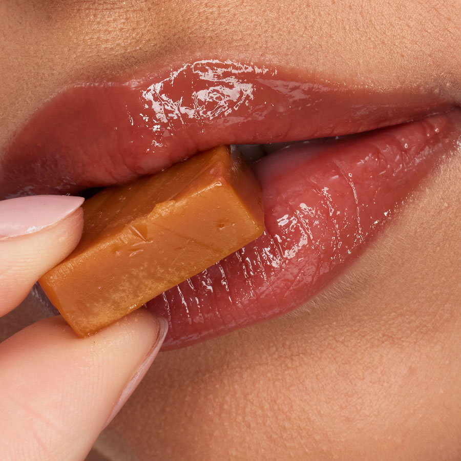 Close-up lips wearing YSL LOVESHINE CANDY GLAZE biting caramel candy.
