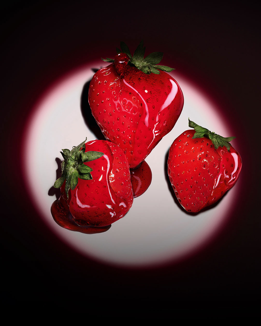 Three fresh red strawberries highlighted by a pink circular spotlight on a dark background.