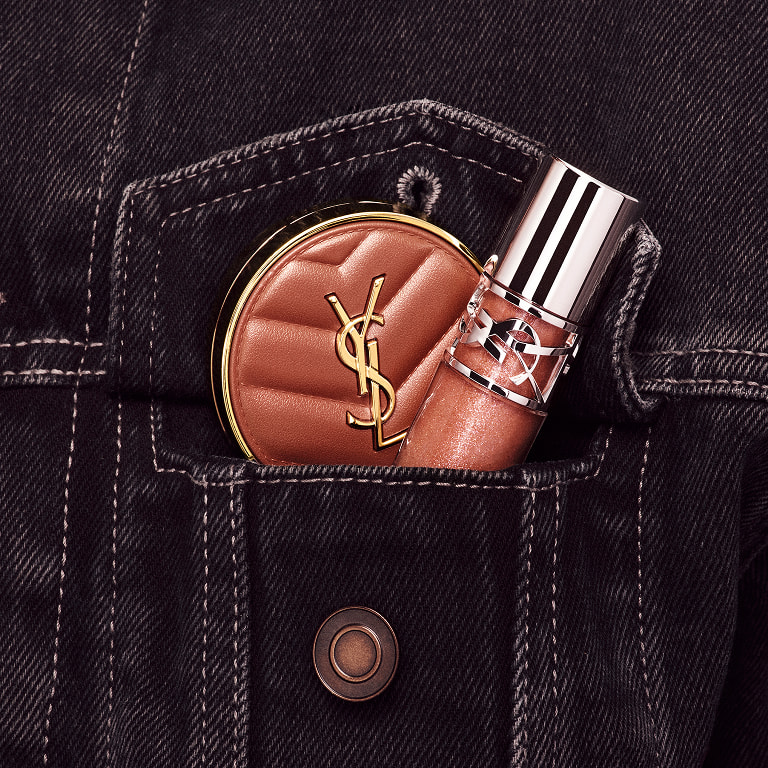 Hand placing YSL LOVESHINE Lip Oil Gloss and pink Make Me Blush
compact into a denim pocket in shade Honey Moon.