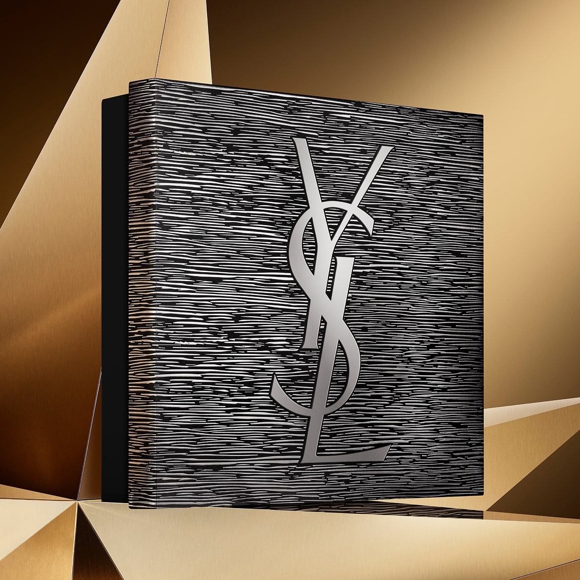 Holiday gift set in silver and black tones, featuring the YSL Beauty logo, on a golden geometric background.