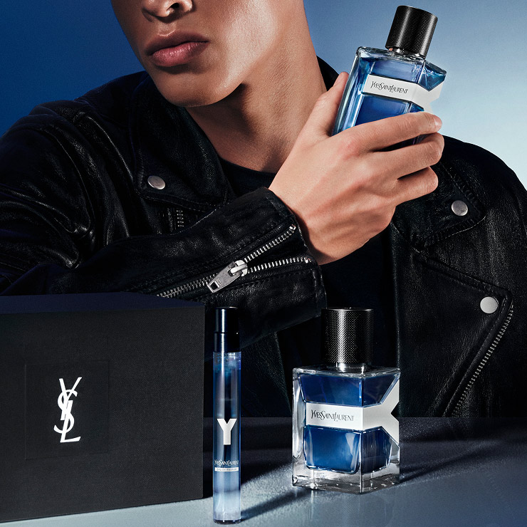 A man, in a leather jacket, holds YSL Y EDT Intense Iced Cologne, with a YSL gift box and travel spray.