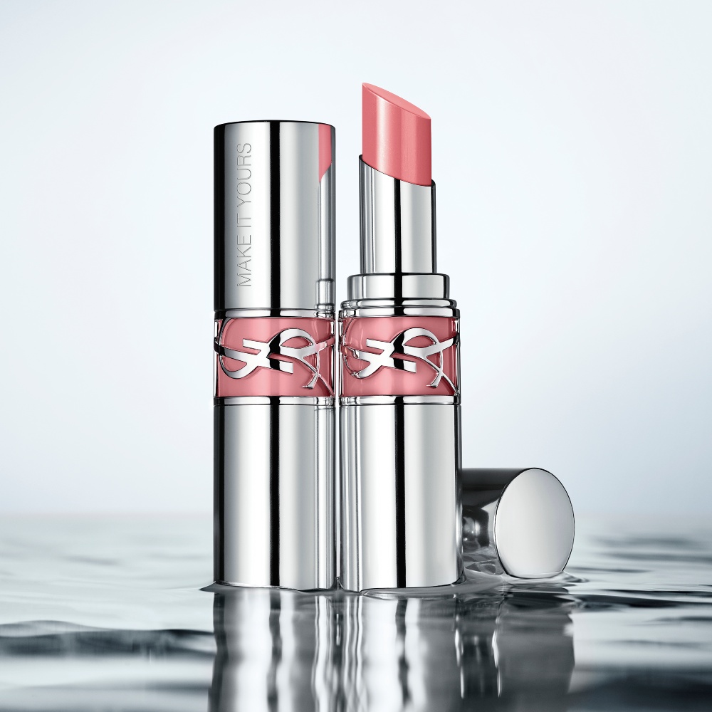 Two YSL LOVESHINE Lipsticks, one open pink, one closed with 'MAKE IT YOURS' engraving, on a reflective water surface.